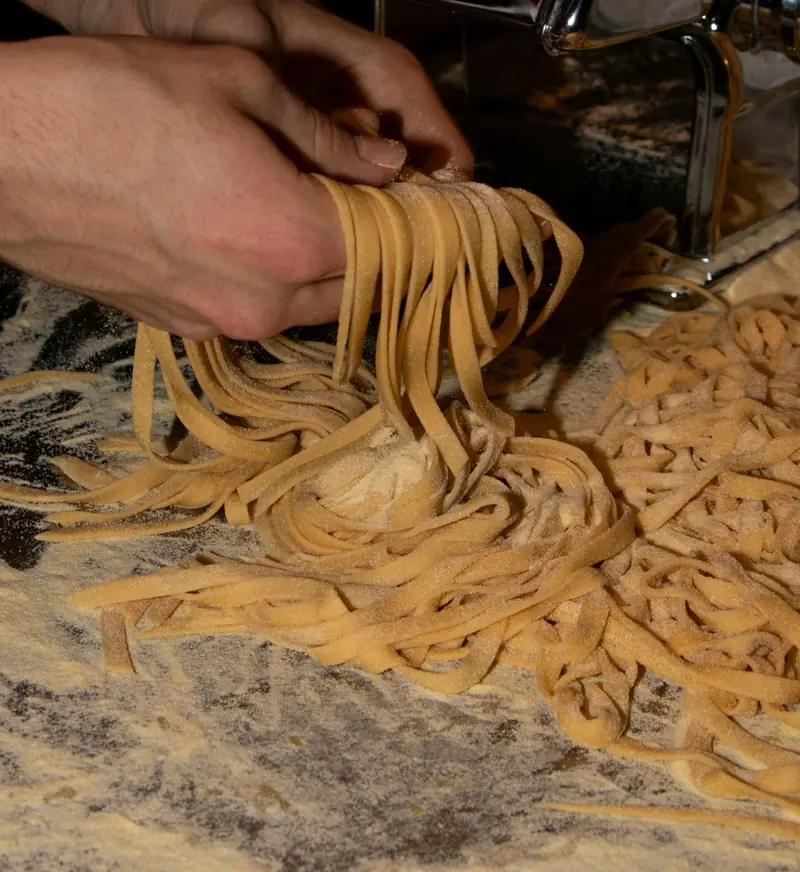 Due mani raccolgono le tagliatelle appena tirate su un piano infarinato.