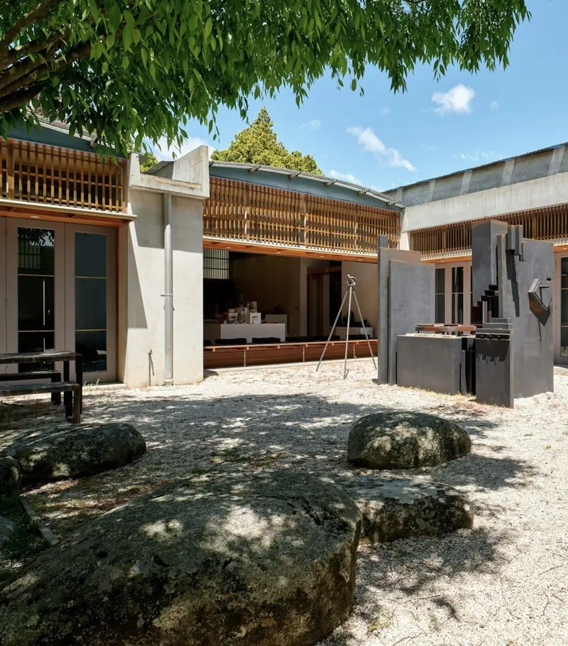 Il portico in larice con i frangisole a listelli, la scultura e i grandi massi nella ghiaia.