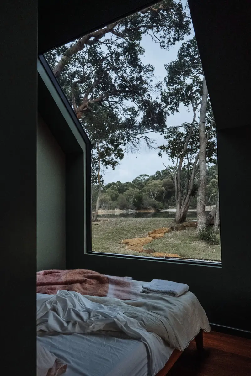 Letto in una nicchia dalle pareti scure, con una finestra a tutta altezza sugli alberi.