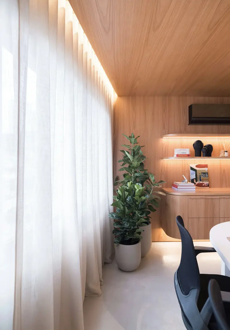 Tende in lino a tutta altezza lungo la facciata, soffitto in rovere con luce radente e mensole illuminate.