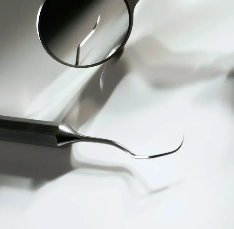 Specchietto e sonda odontoiatrica in acciaio su un piano bianco.
