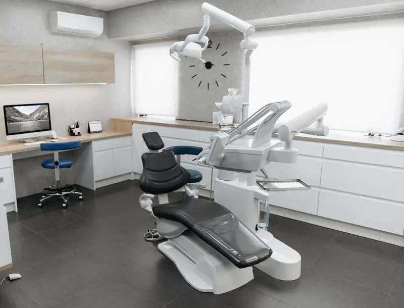 Ambulatorio con poltrona, riunito, mobili bianchi e postazione con monitor per la cartella clinica.