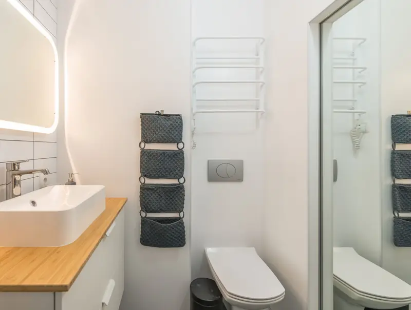 Piccolo bagno bianco con sanitari sospesi, lavabo d'appoggio su piano in bambù e specchio retroilluminato.