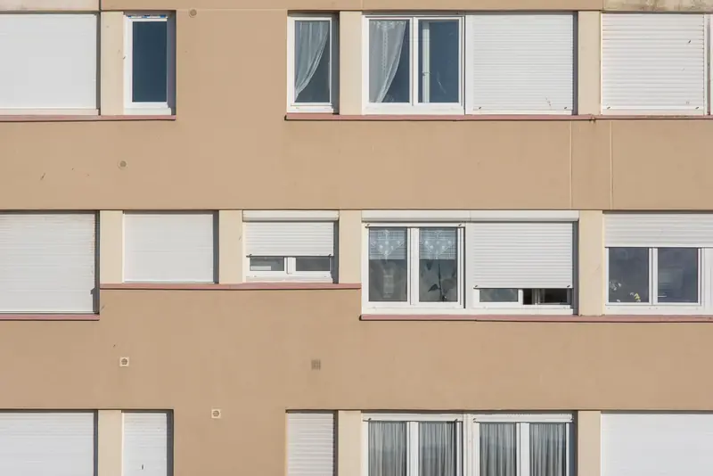Facciata di un condominio dopo il cappotto termico e la tinteggiatura color sabbia, con nuove tapparelle bianche.