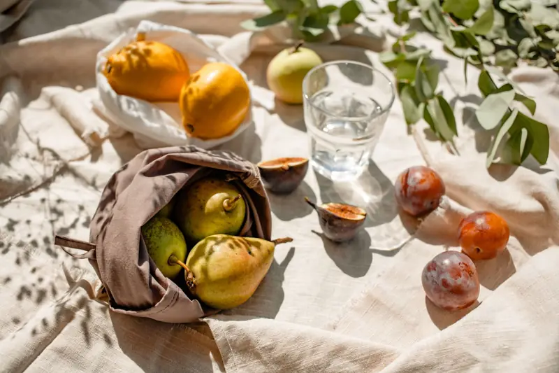 Pere, susine, fichi aperti e un bicchiere d'acqua su una tovaglia di lino, nella luce del mattino.