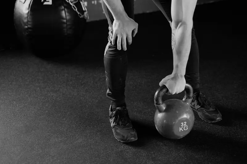 Una mano afferra un kettlebell appoggiato sul pavimento della sala.