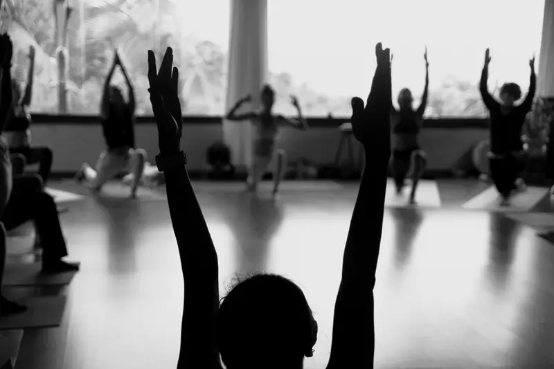 Una lezione di yoga in controluce: braccia alzate davanti alle vetrate della sala.