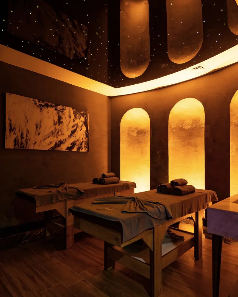 Cabina per due con due lettini da massaggio, nicchie ad arco illuminate e luce calda.