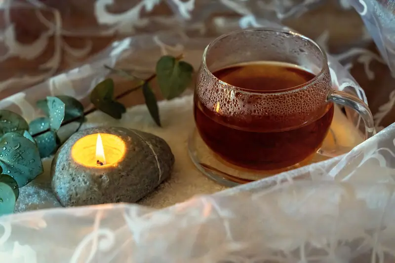Una tazza di tisana calda accanto a una candela accesa in una pietra e a rametti di eucalipto.