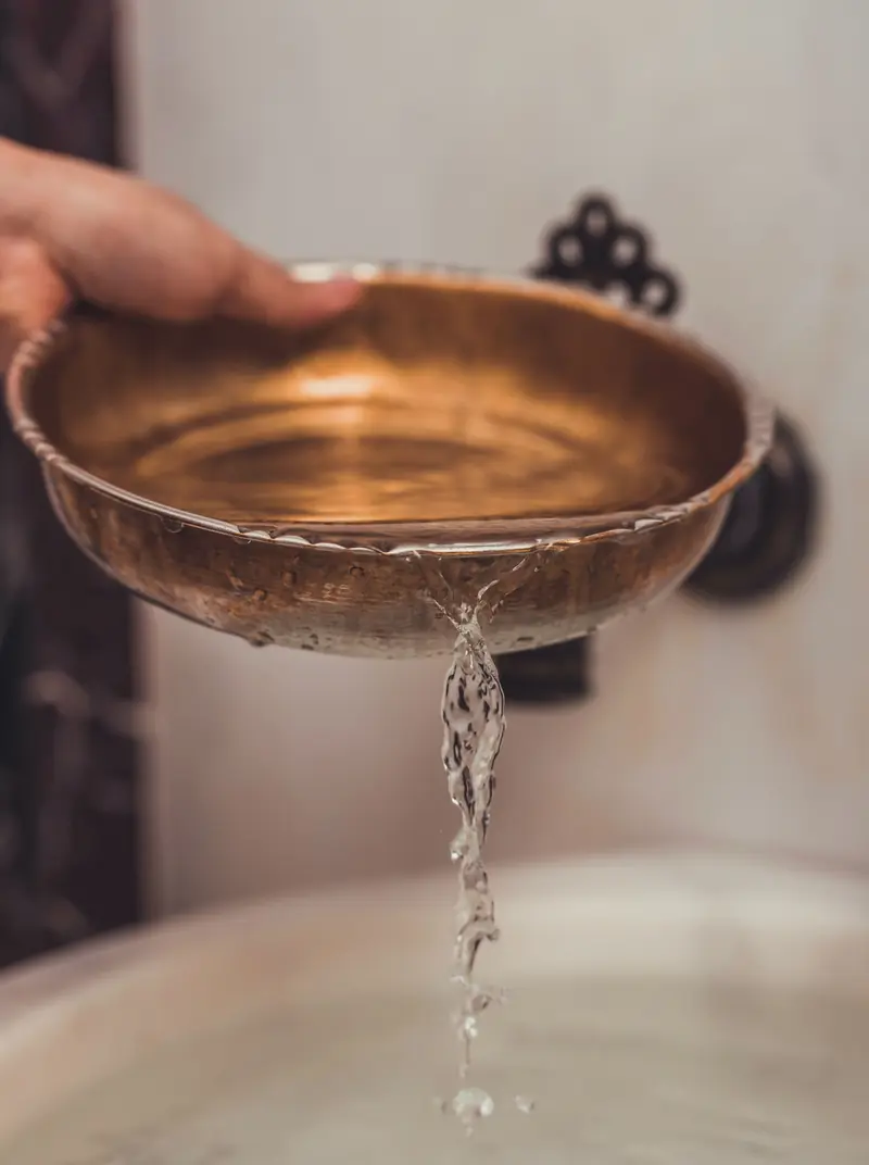 Una ciotola di rame versa un filo d'acqua in un lavabo di marmo.