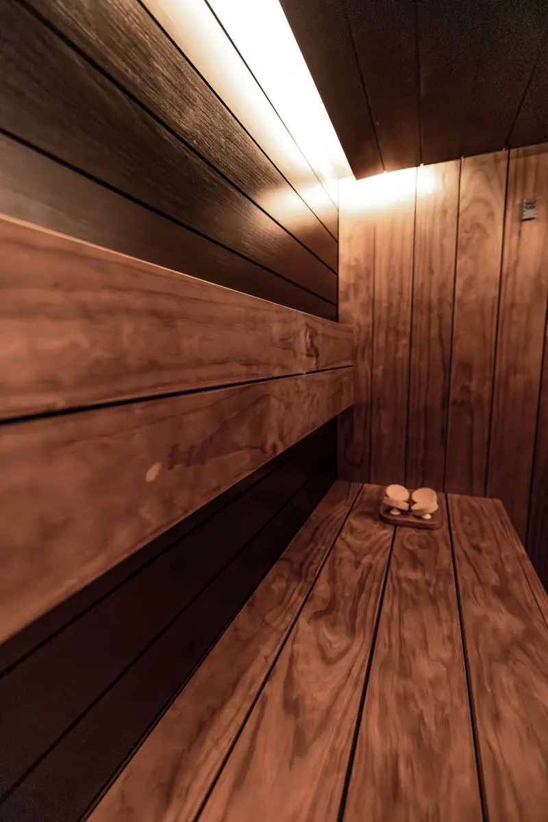Sauna in legno scuro con una lunga panca e una luce calda sotto il soffitto.