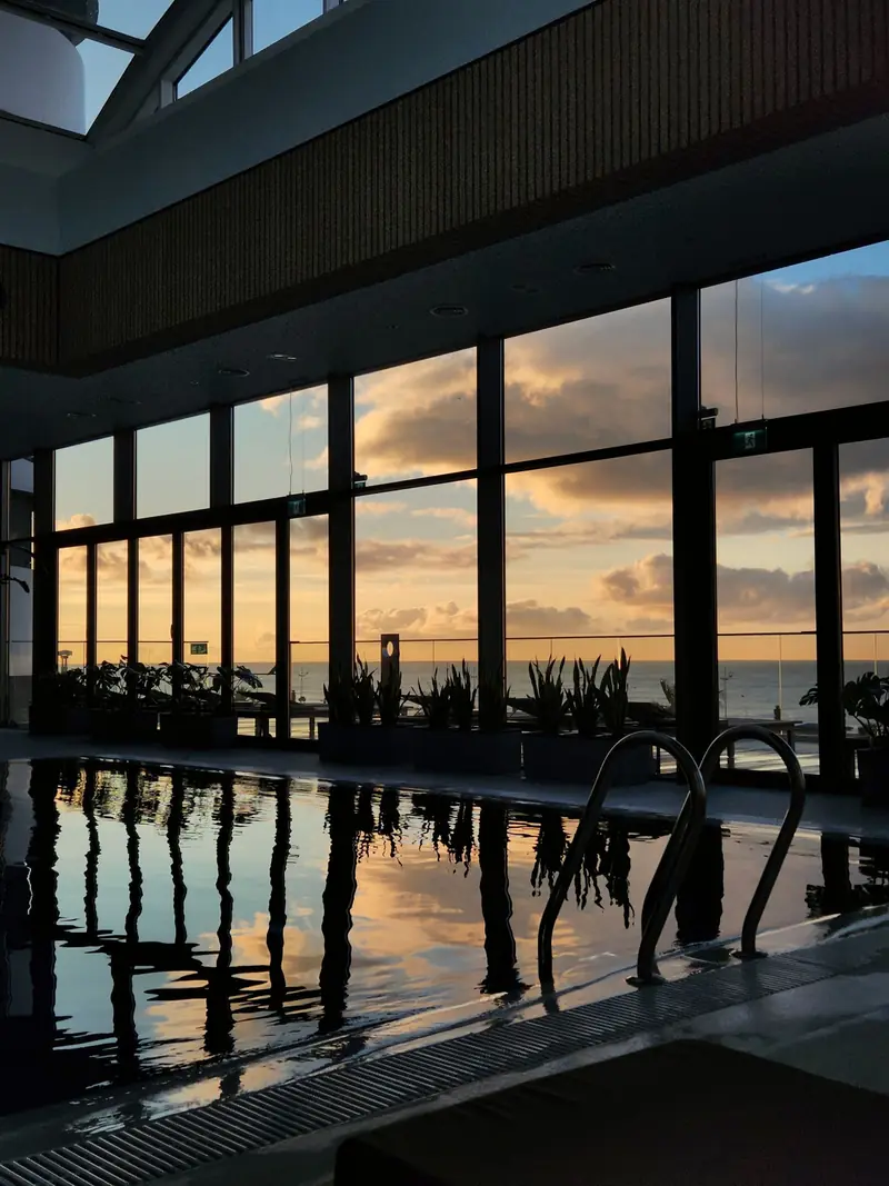 Piscina interna al tramonto, con una grande vetrata che si riflette nell'acqua.