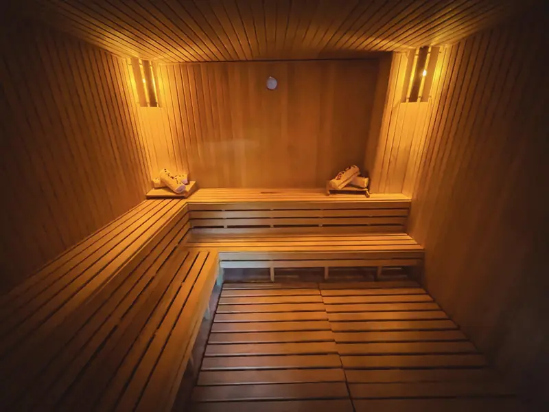 Sauna in legno chiaro con panche a gradoni e luci ambrate alle pareti.