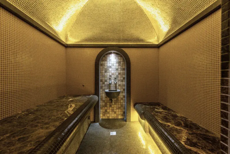 Bagno turco a volta rivestito di mosaico dorato, con due sedute di pietra e una nicchia ad arco.